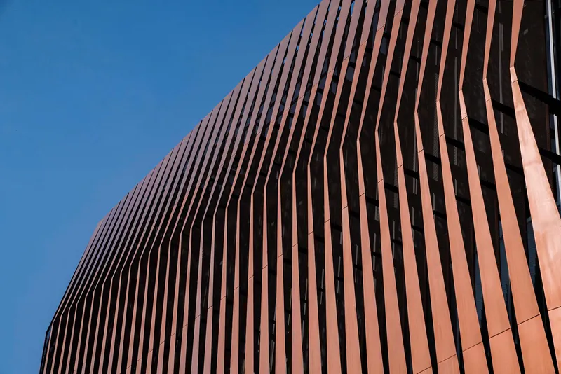 Curved copper-toned vertical fins wrapping the podium facade against clear sky
