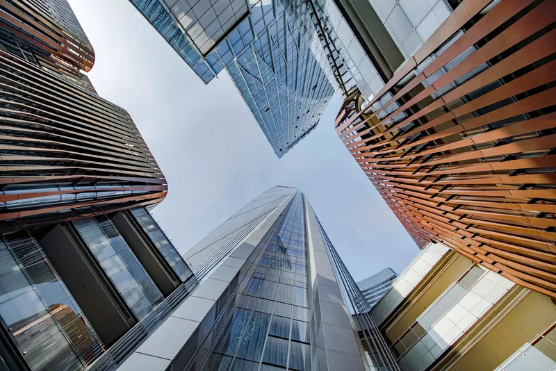 Upward perspective showing glass towers and ribbed facades meeting at a plaza courtyard