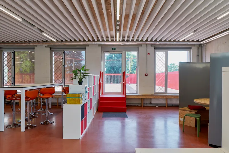 Open interior with linear baffle ceiling, red rubber flooring, and glass doors leading to an exterior terrace