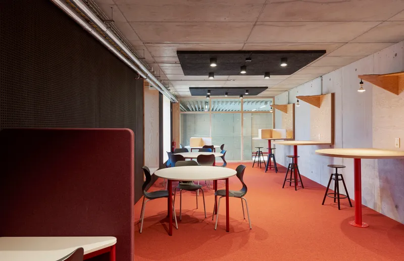 Casual seating area with terracotta flooring, perforated acoustic wall panels, and timber-framed glass partitions beyond