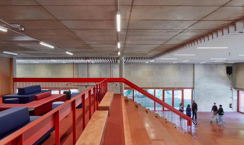 Upper level mezzanine with red steel railing, cork flooring, and figures moving through the entry hall below