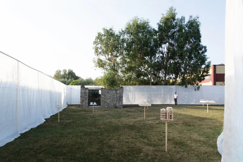 Courtyard with white fabric screens, stone ruin, and a visitor standing on grass at dusk