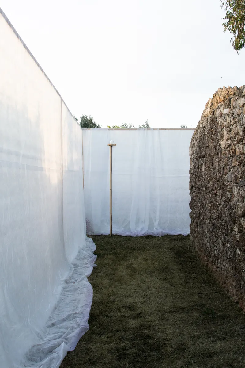 Narrow passage between white fabric screen and rough stone wall with timber prop