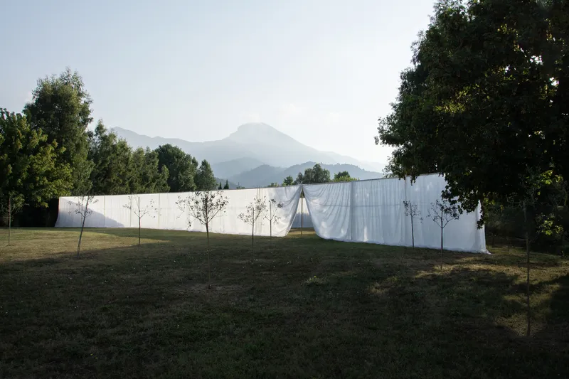 Long white fabric barrier stretched across a grassy field with mountain peaks in the distance