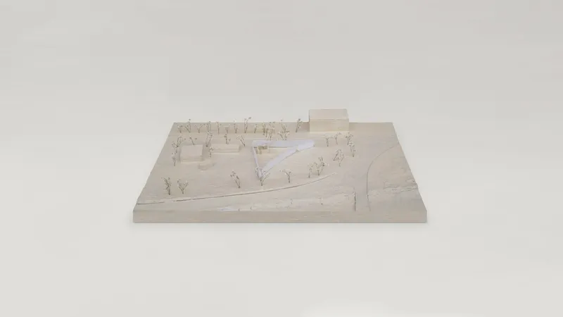 Physical model showing a triangular pavilion in a landscape with miniature trees and pathways