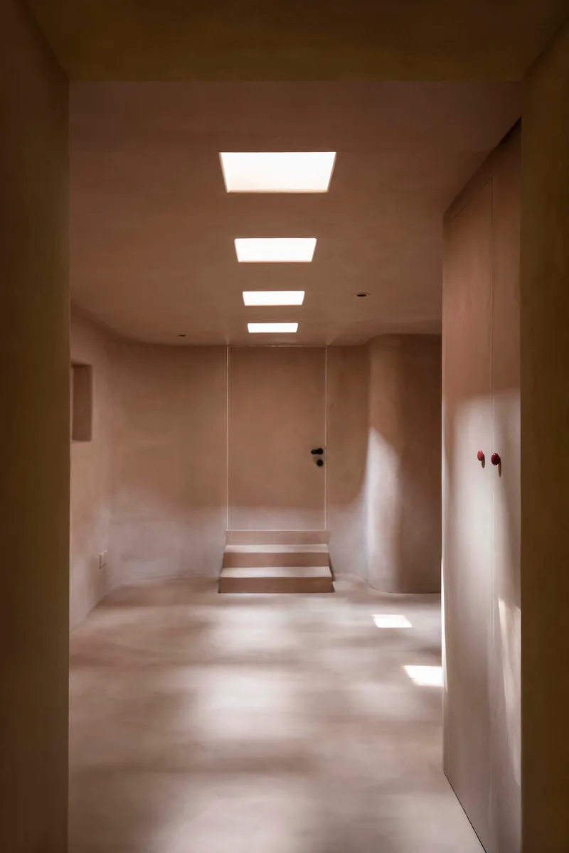 Corridor with four recessed ceiling lights illuminating plastered walls and a stepped threshold ahead