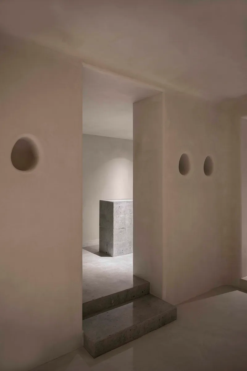 Interior threshold with concrete steps connecting plastered rooms punctuated by oval wall sconces