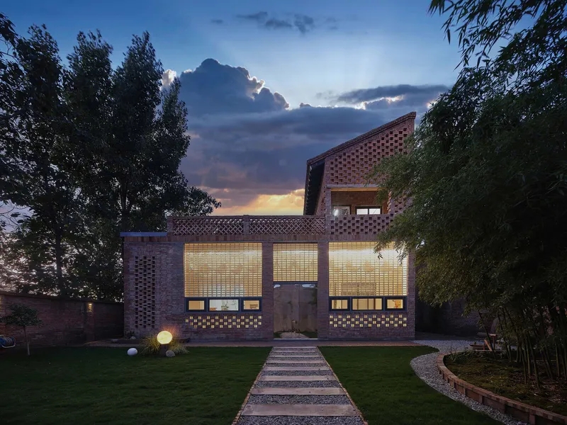 Front facade with perforated brick walls and illuminated glass block windows at dusk beneath dramatic clouds
