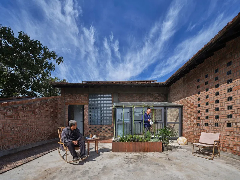 Courtyard terrace with planted bed in metal planter and two seated figures beneath open sky