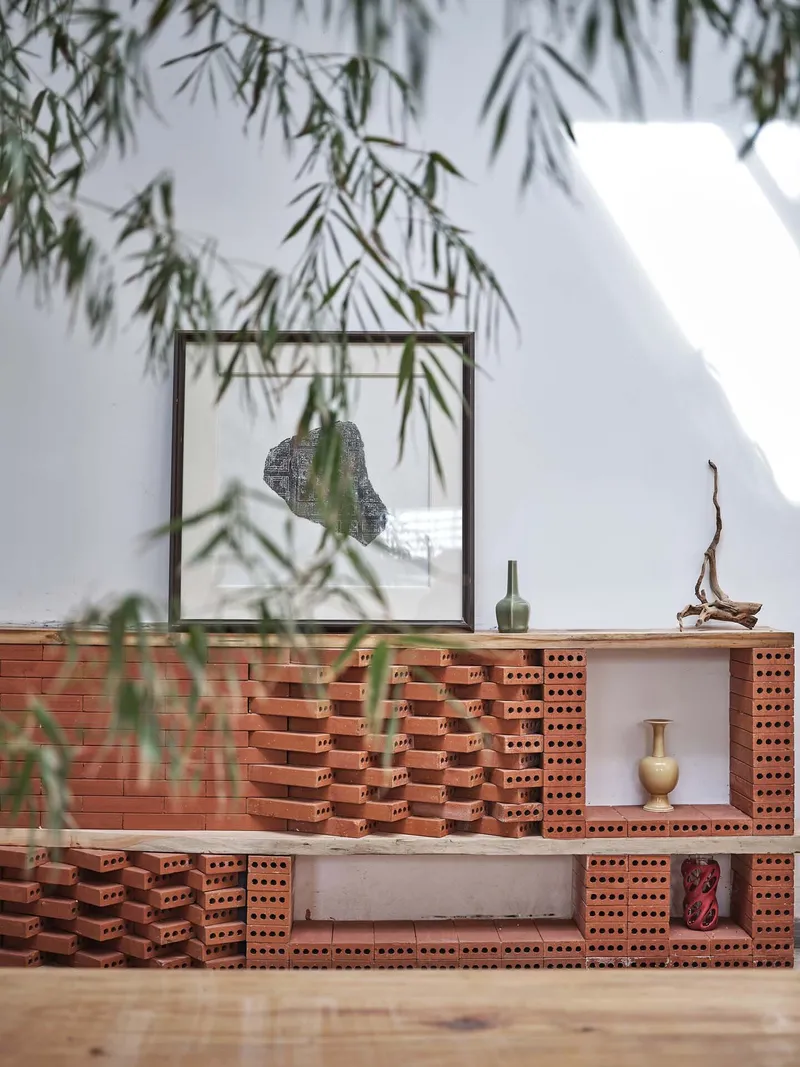 Tiered display platform built from perforated red bricks beneath overhanging bamboo foliage
