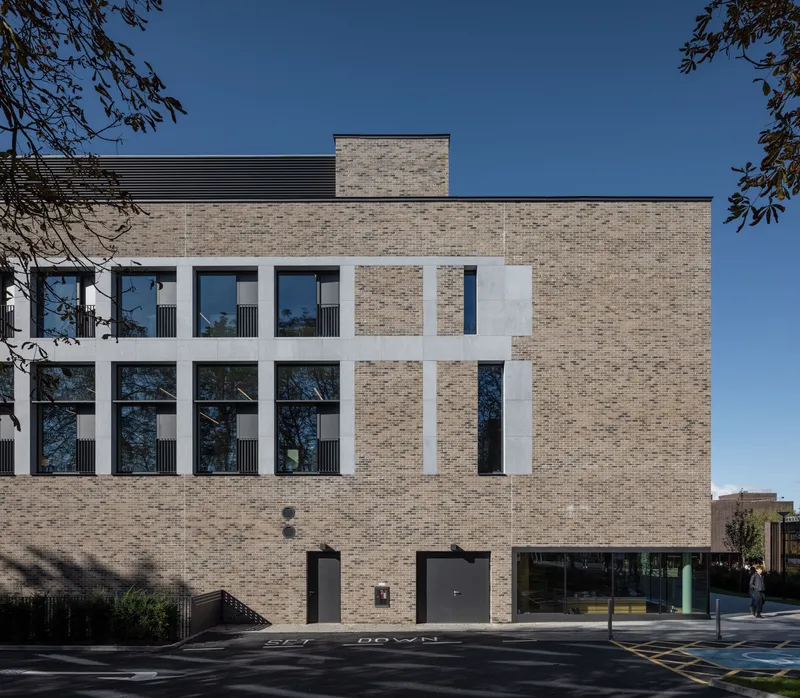 Street facade with pale brick and recessed white concrete frames around tall windows beneath a blue sky
