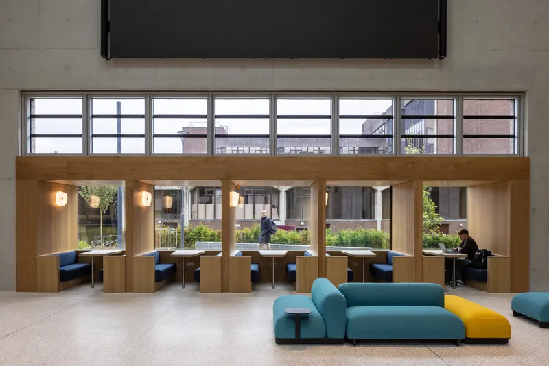 Row of timber framed study alcoves with built-in desks and banquette seating overlooking a planted courtyard