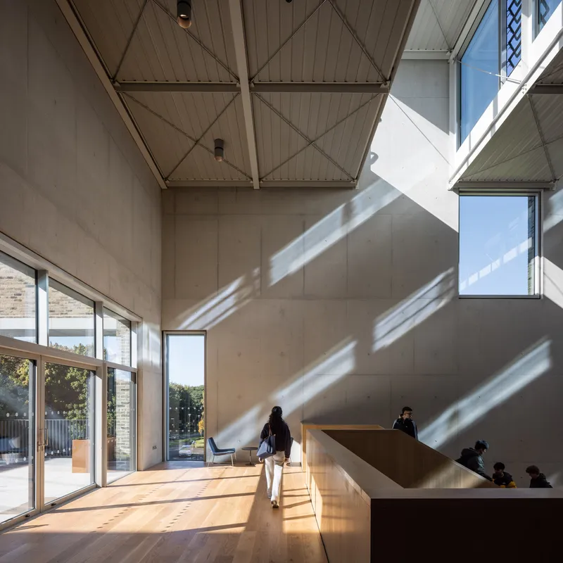 Interior circulation corridor with angled sunlight patterns crossing concrete walls and timber ceiling structure