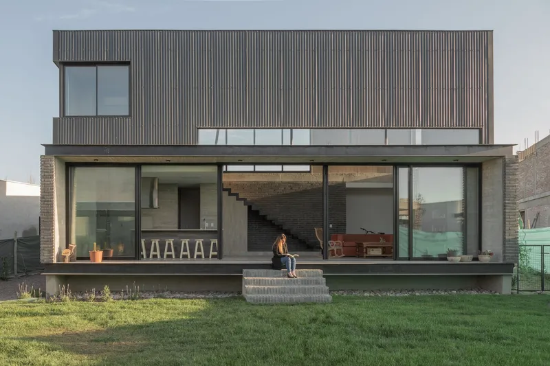 Rear facade with vertical timber cladding above a glazed ground floor with a person seated on the terrace