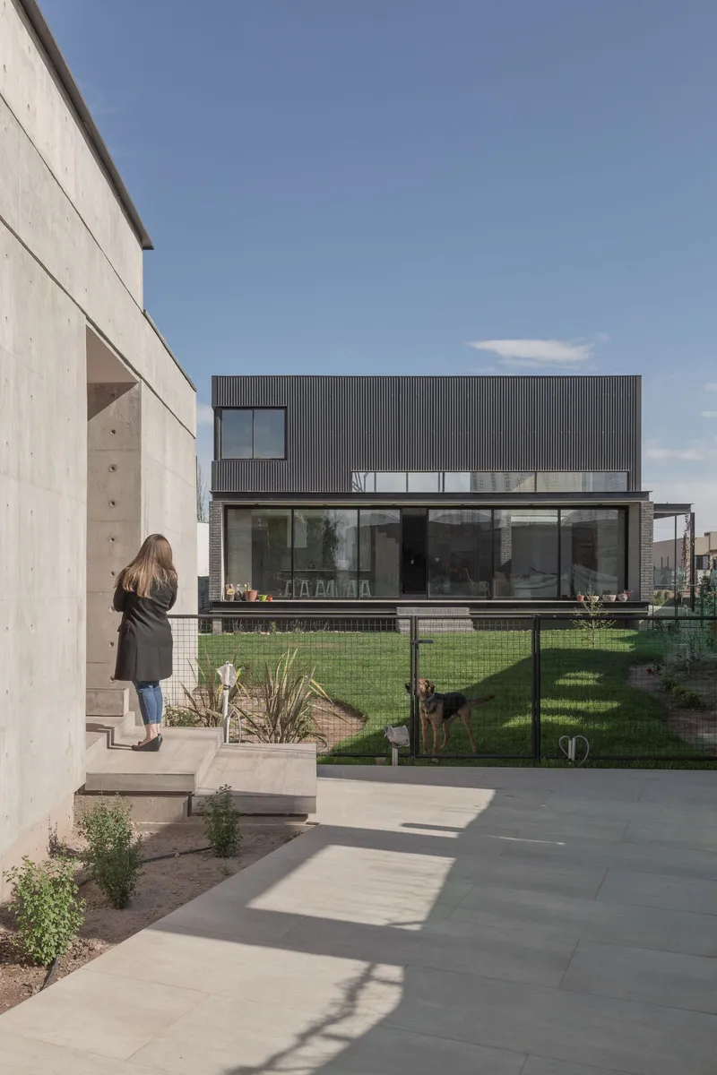 Concrete patio with large pavers leading to the glass-walled rear facade as a person walks down the steps