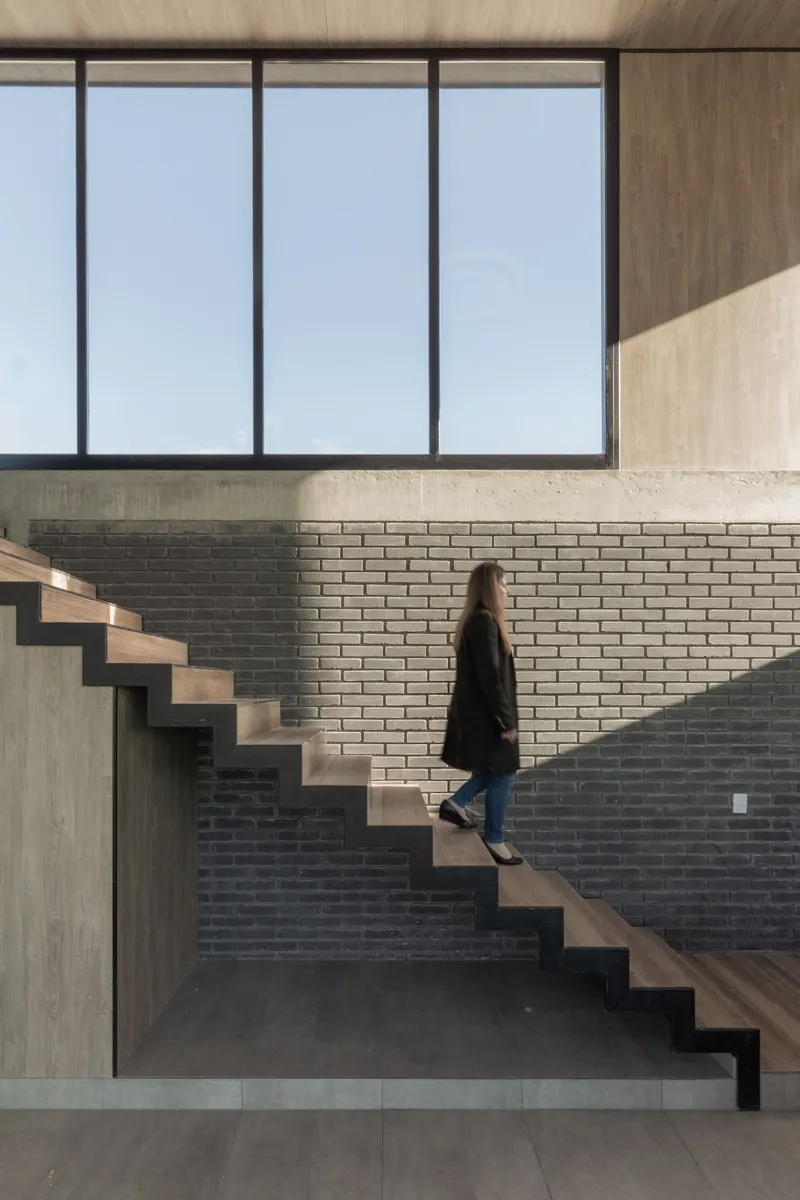 Cantilevered timber staircase against a brick wall with a person ascending toward the glazed upper level