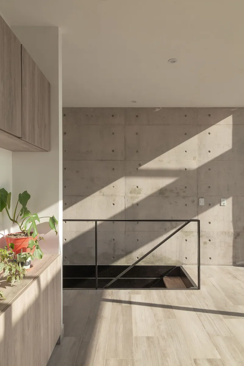 Board-formed concrete wall with diagonal shadows from sunlight streaming across the light wood floor