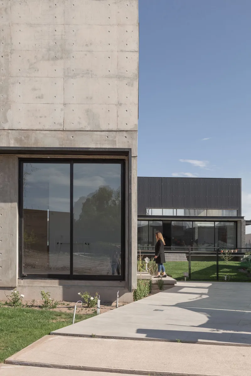 Concrete volume with floor-to-ceiling glazed door as a figure walks along the curved pathway