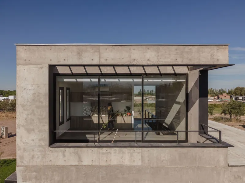 Glazed bay window projecting from board-formed concrete volume with metal canopy and afternoon shadows