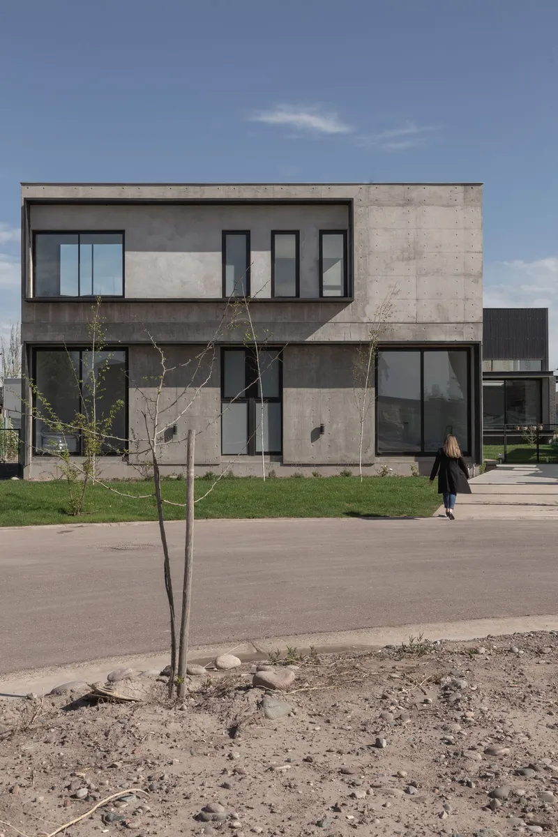 Street view of the two-storey board-formed concrete facade with young trees and figure approaching