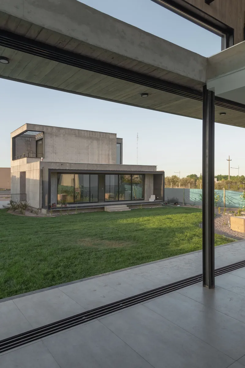 View through concrete overhang framing adjacent house volumes across lawn at golden hour