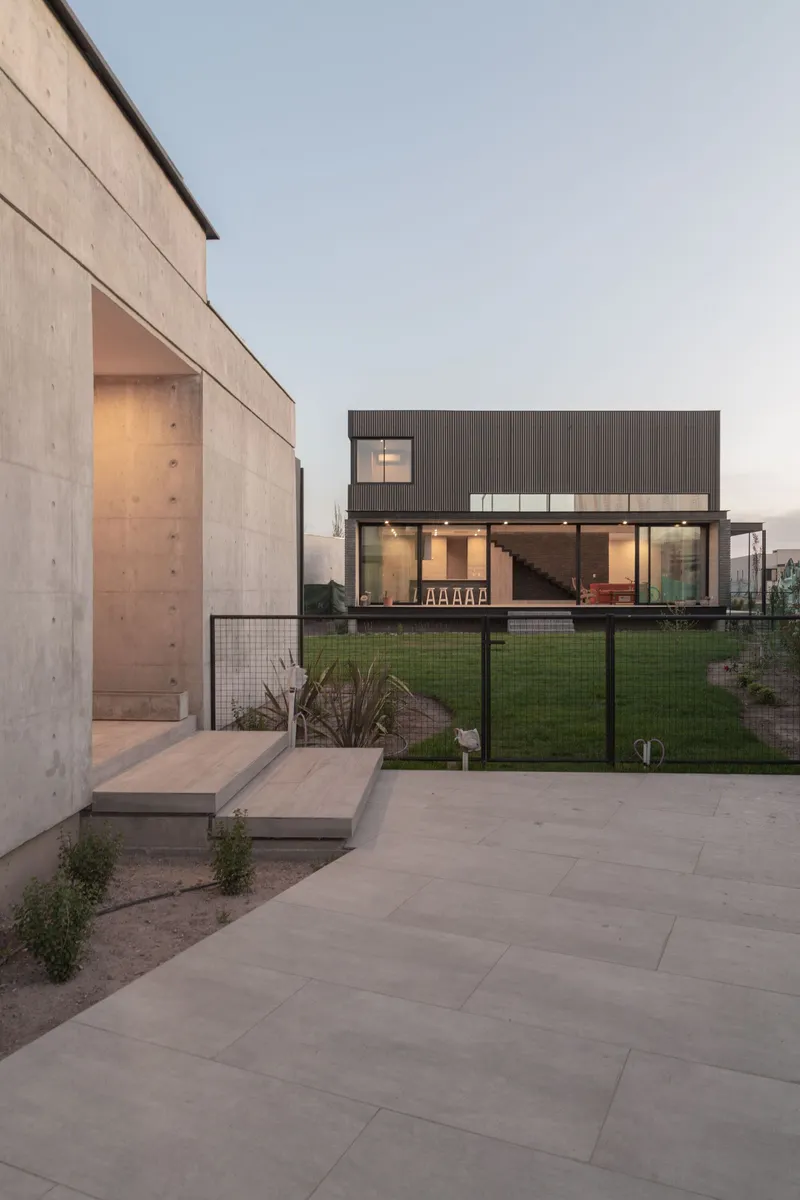 Evening view across the paved terrace showing the glazed living area and concrete wall volumes