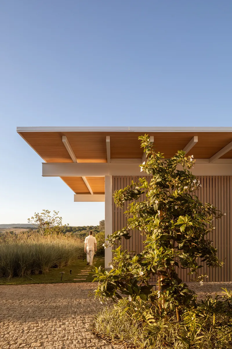 Overhanging timber roof with exposed beams above vertical slat facade and a figure walking at dusk
