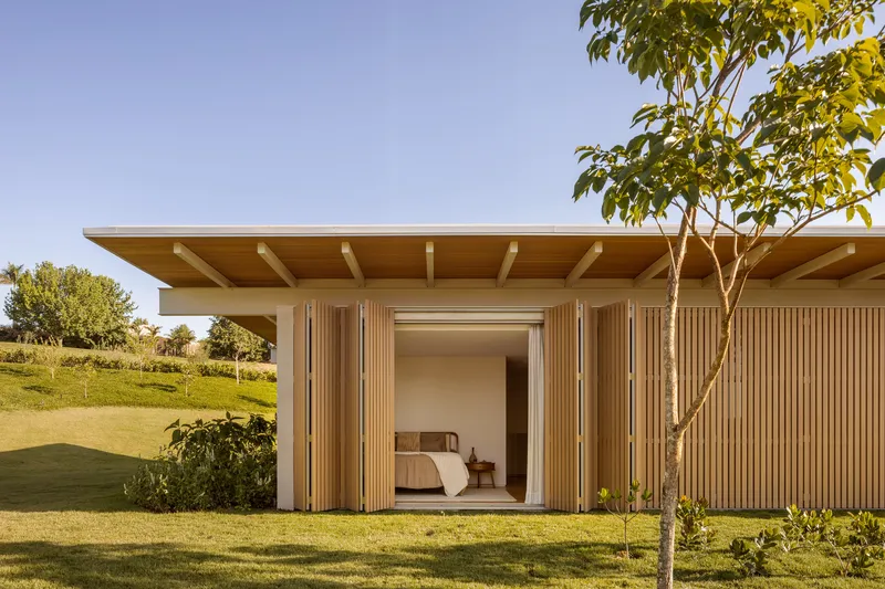 Bedroom glimpsed through folding timber slat doors framed by a young tree and lawn
