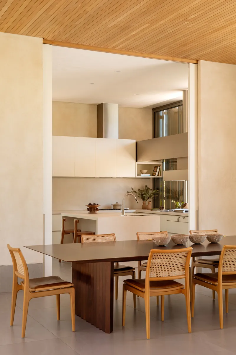 Dining area with cane chairs beneath timber ceiling beams looking through to the kitchen beyond