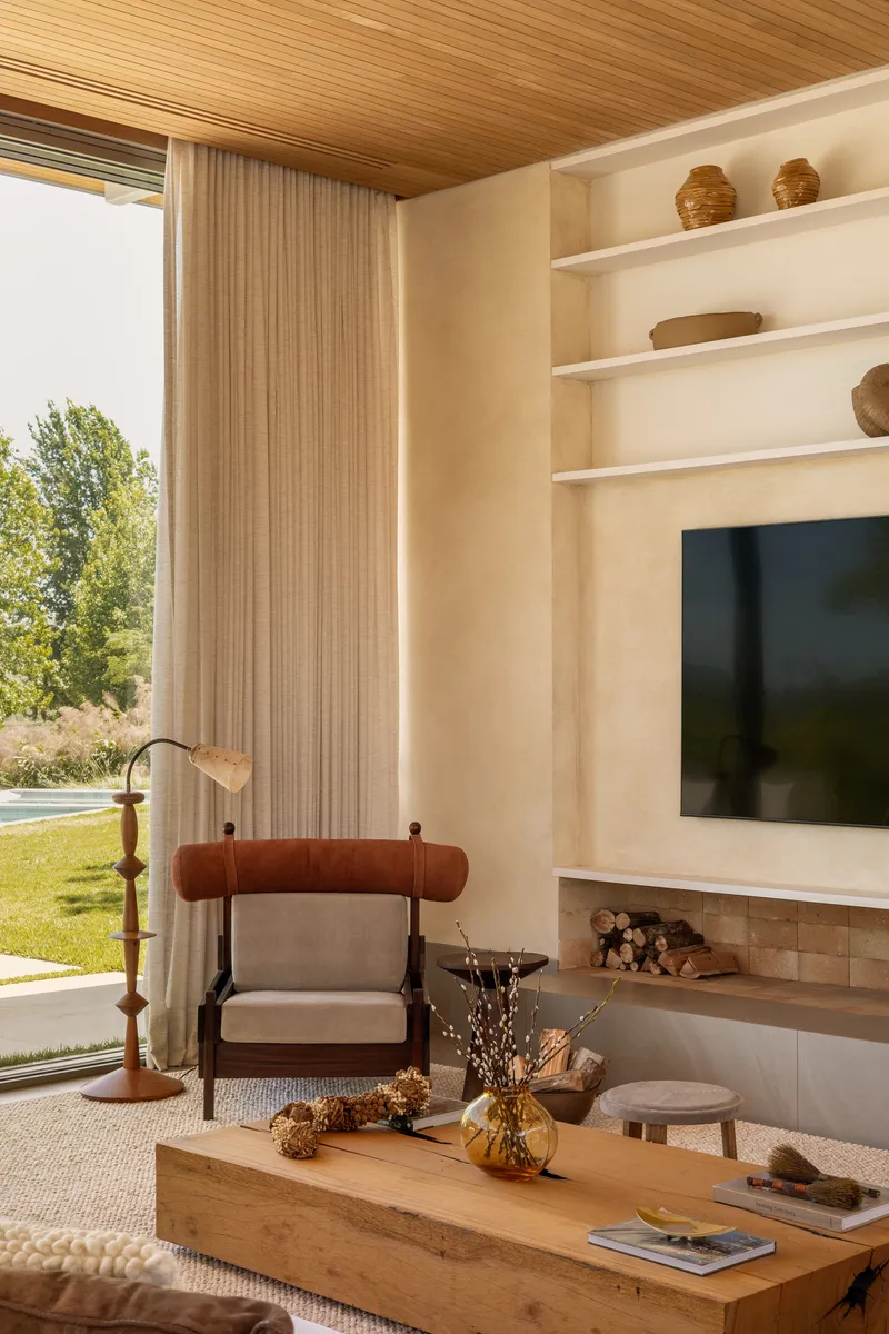 Living room with timber ceiling, built-in shelving, and floor-to-ceiling windows overlooking lawn in afternoon light