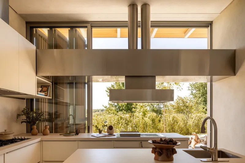 Kitchen island with stainless steel range hood beneath clerestory windows framing trees beyond