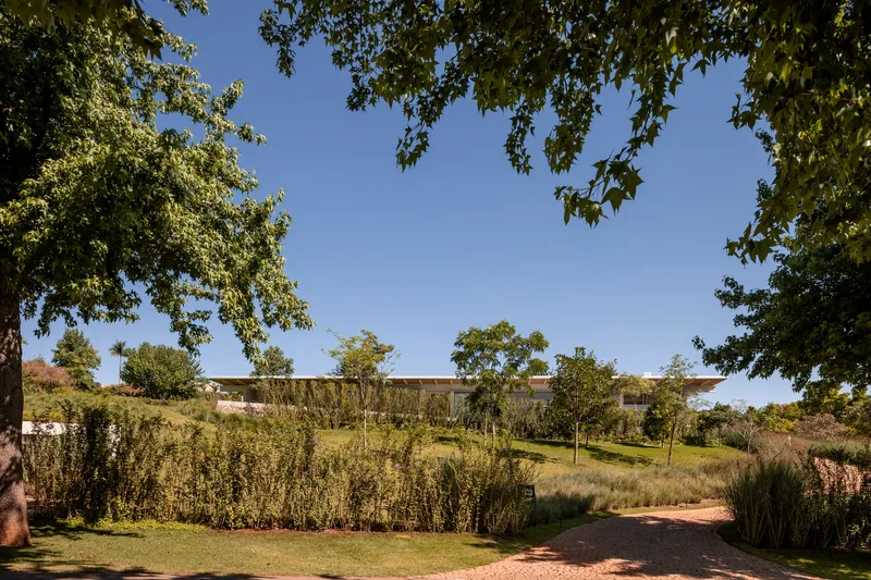 Low-slung horizontal roofline seen from a gravel path through planted gardens and mature trees