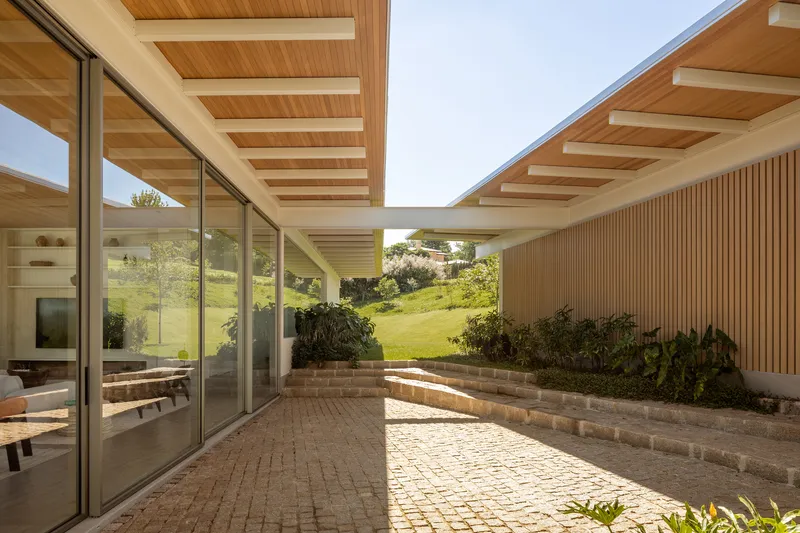 Brick-paved courtyard framed by timber slatted walls and floor-to-ceiling glass under exposed beam ceilings