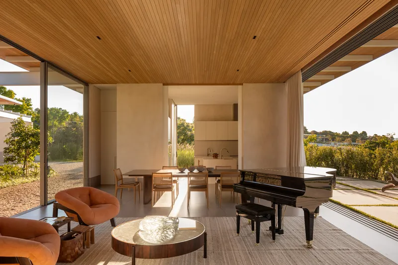 Living and dining room with timber slat ceiling and grand piano bathed in afternoon sunlight