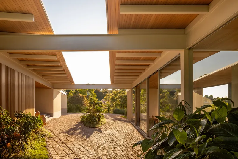 Covered courtyard walkway with rectangular skylights and timber beams framing views to planted beds