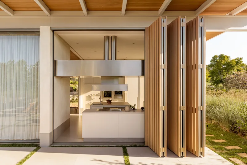 Folding timber screen panels opening the kitchen to a terrace with grass joints at dusk