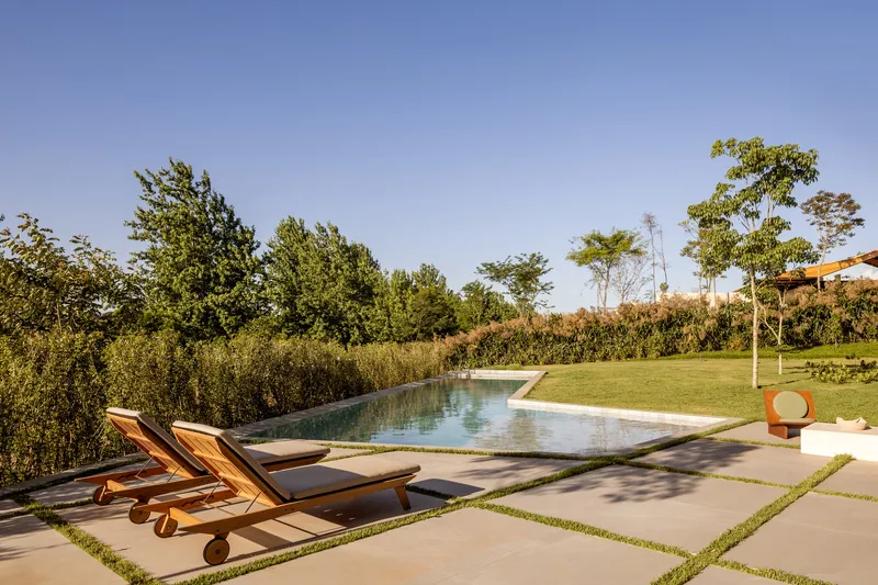 Swimming pool with stone coping and timber loungers beside lawn and planted hedgerow