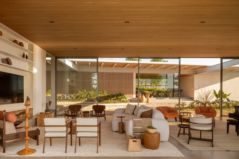 Open-plan living room with wood slat ceiling and full-height glazing overlooking an interior courtyard with planted beds