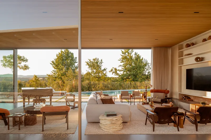 Interior view through glazed walls to terrace with swimming pool and rolling hills beyond at sunset