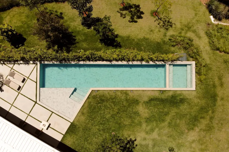 Aerial view of rectangular lap pool with concrete deck surrounded by lawn and scattered trees