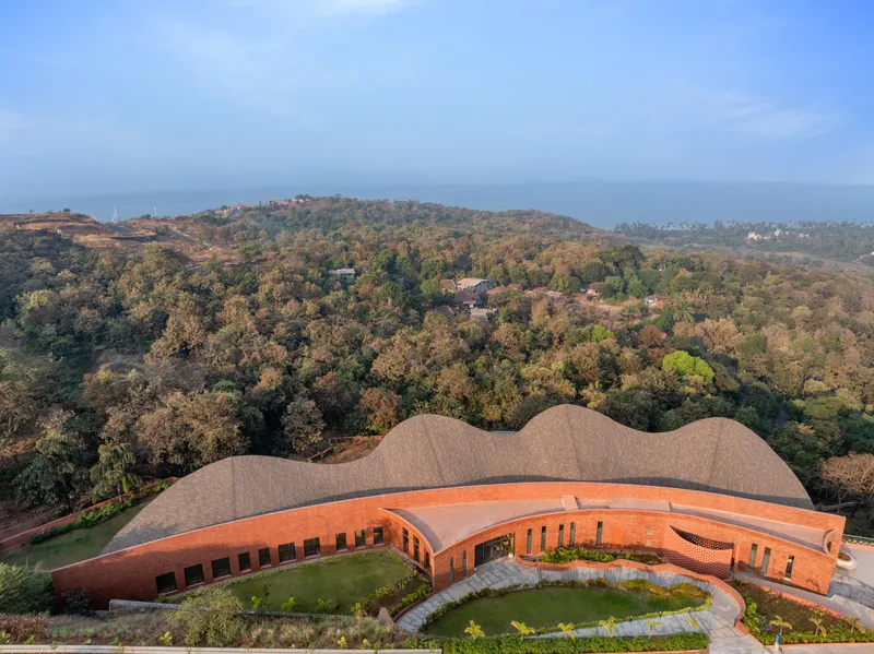 Aerial view of the three-lobed roof form set among forested hills with a central courtyard lawn
