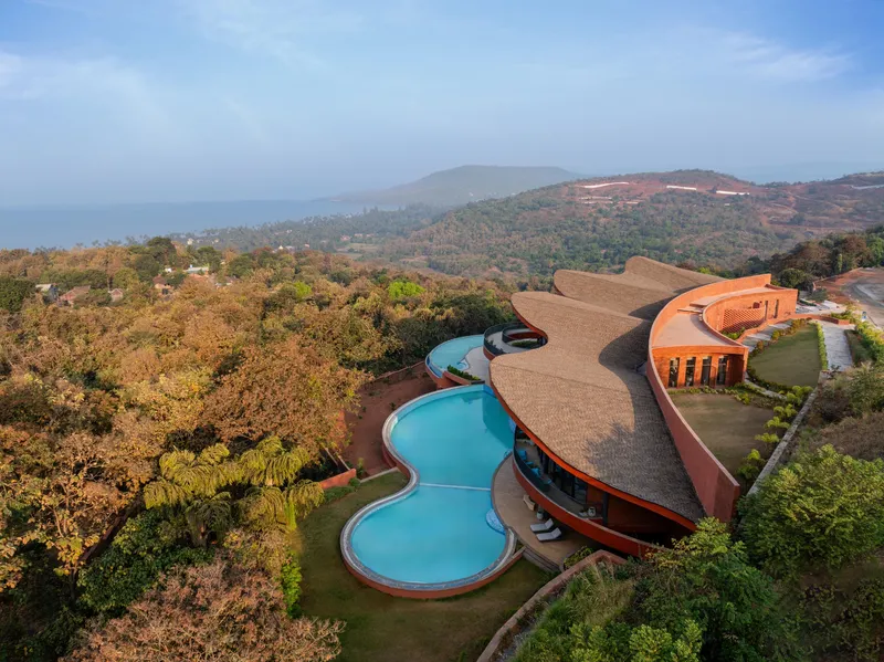 Drone perspective showing the curving pool extending from the terracotta facade into the landscape
