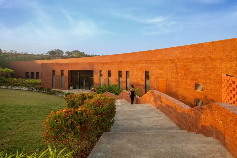 Pathway between the rammed earth wall and planted bed leading to the glass entrance at dusk