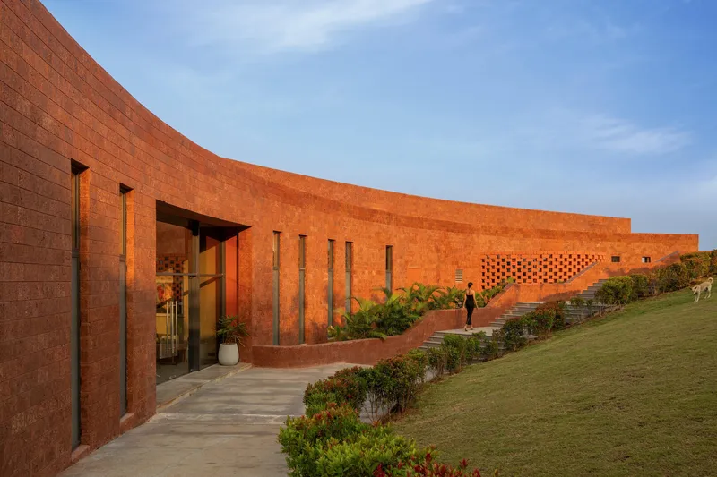 Long view of the rammed earth wall with vertical slot windows at golden hour