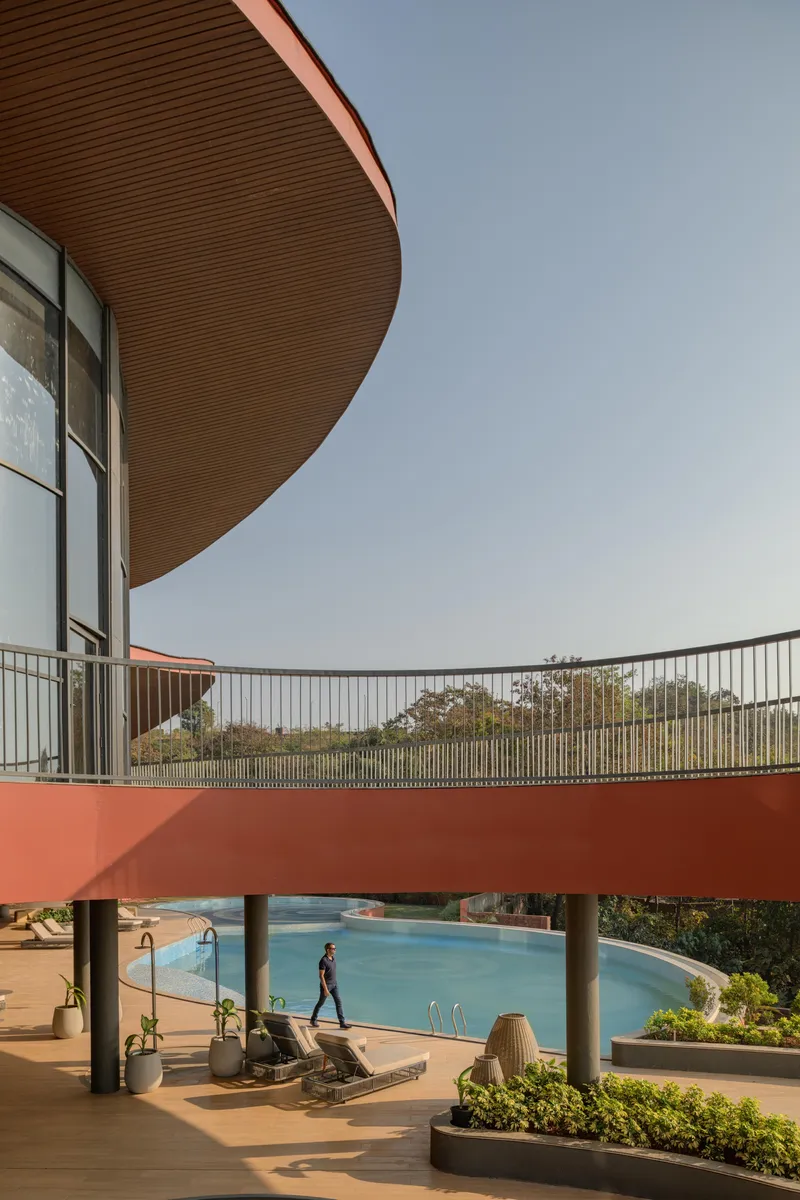 Elevated terrace with curved orange soffit overlooking a swimming pool and visitor walking below