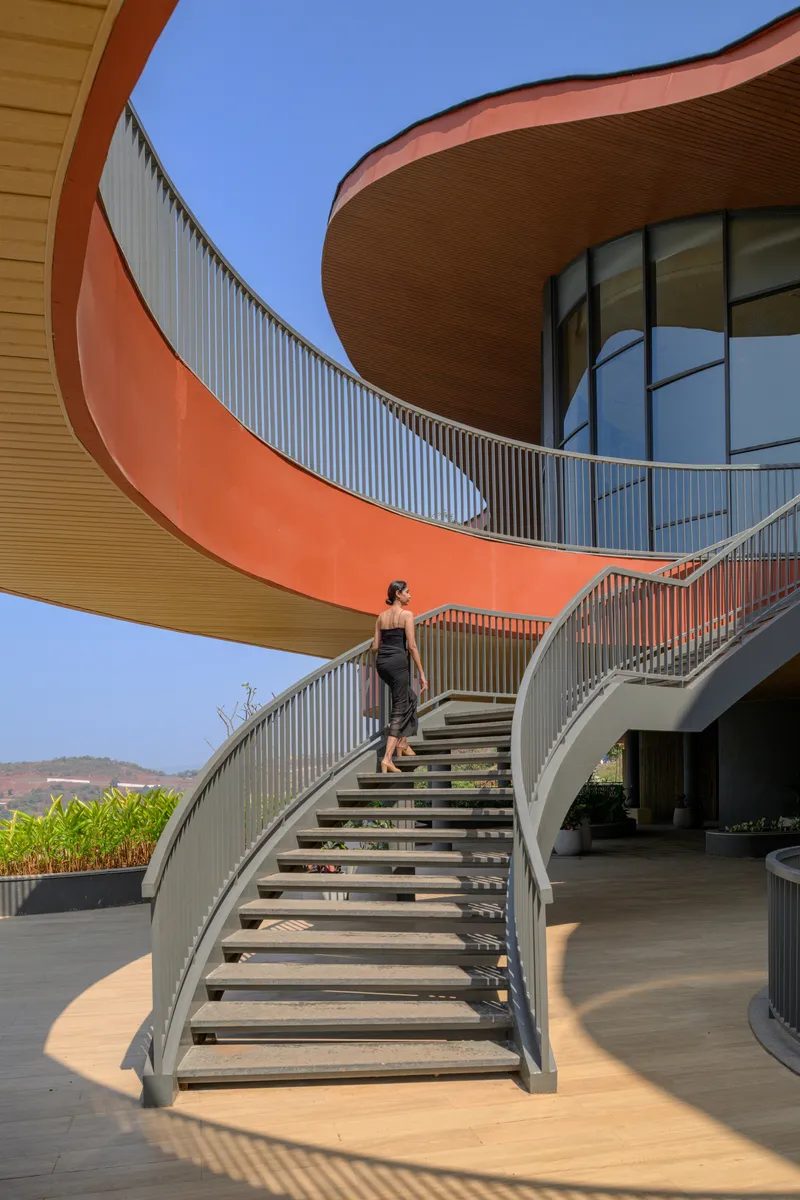 Curved exterior staircase with open risers and a person ascending under blue sky