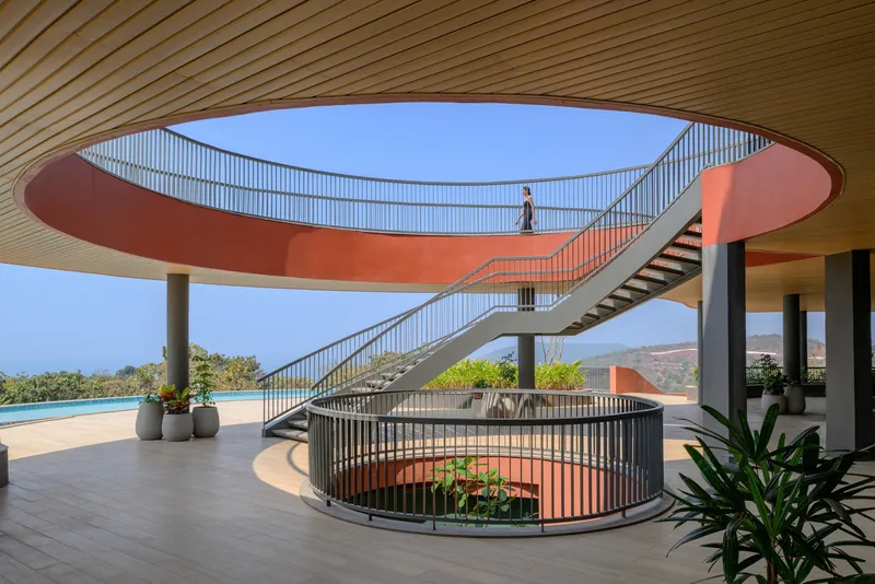 Interior view beneath curved orange bridge linking two levels with spiral staircase and potted plants
