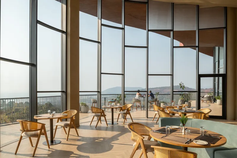 Dining area with timber furniture and floor-to-ceiling gridded windows framing distant hills