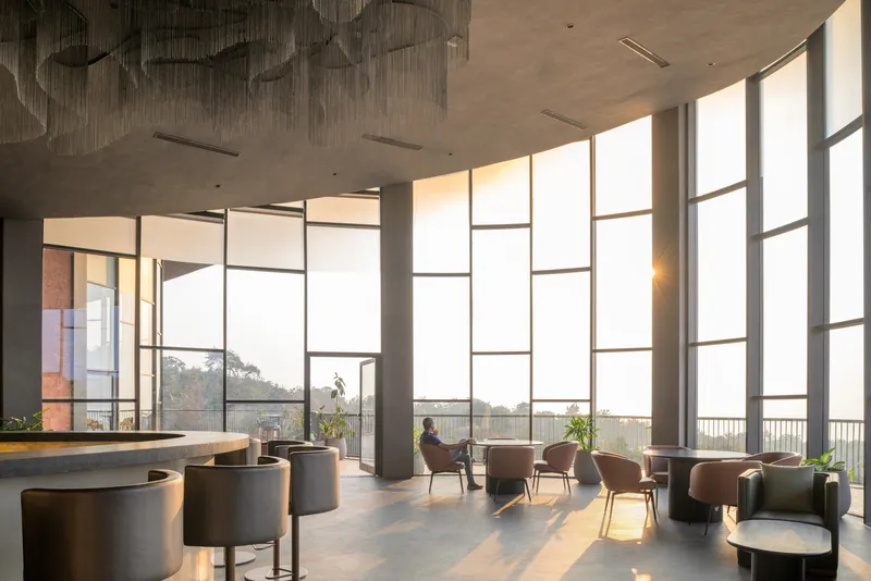 Double-height lounge space with tall gridded windows and afternoon sunlight streaming across seating clusters