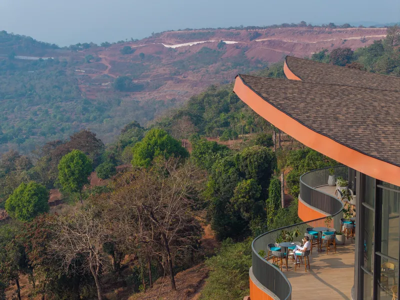 Curved balconies with upturned roof edges extending over a forested hillside landscape